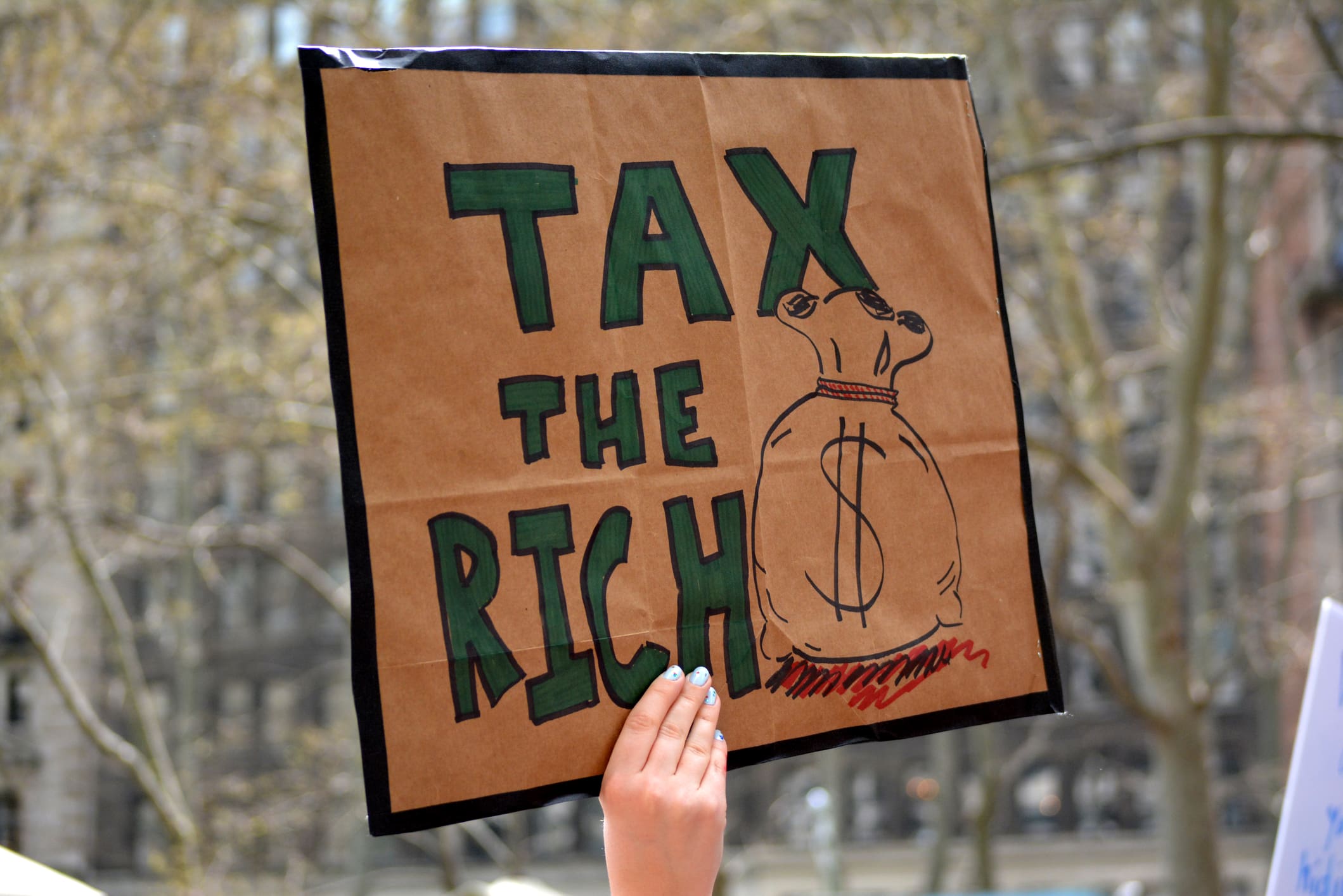A protestor holding a placard that says 'tax the rich'